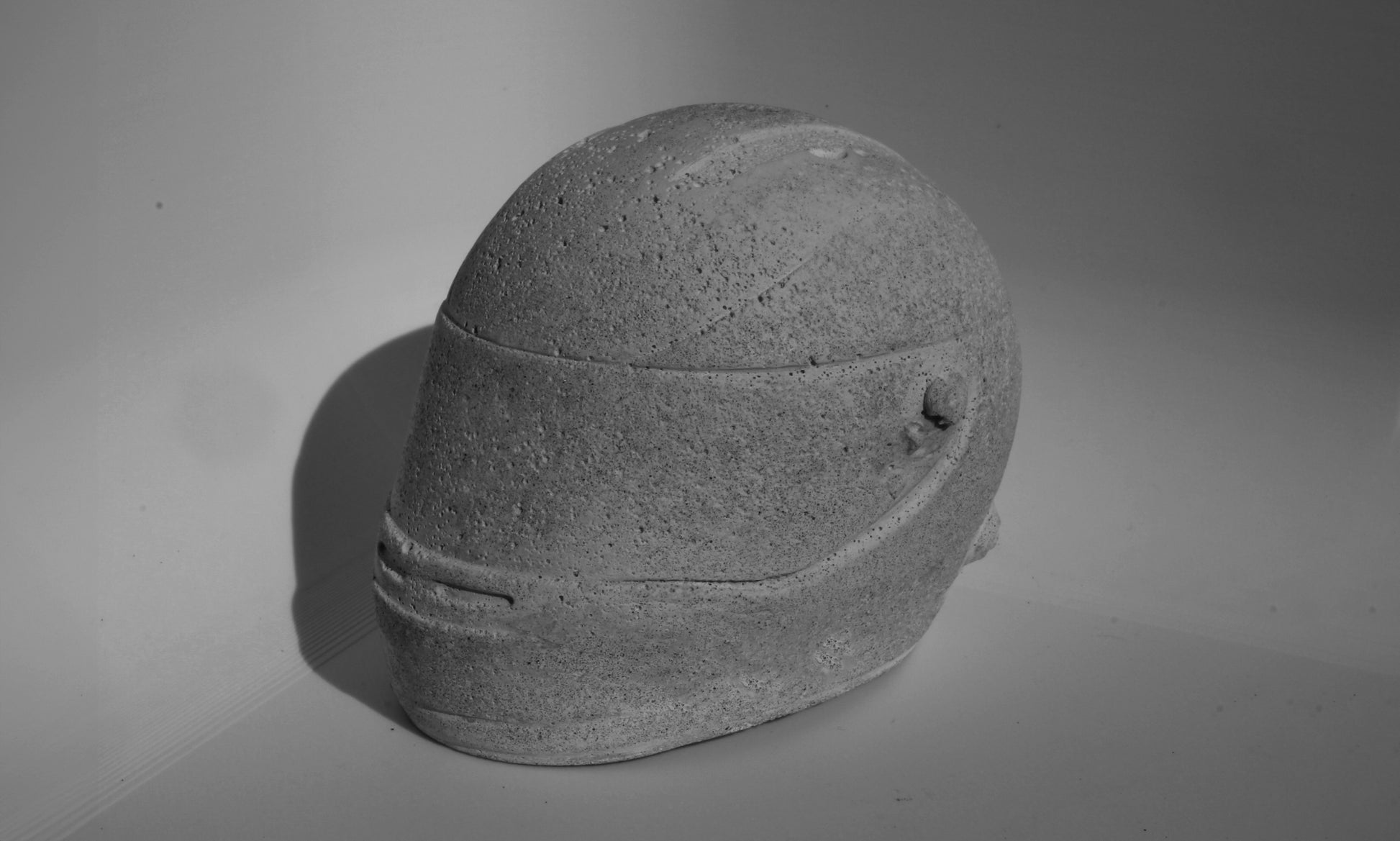 Left side angle of custom-made mini Formula 1 helmet designed with a concrete grey finish, ideal for industrial-style home decor. The helmet, crafted to resemble polished concrete with a matte texture, offers a robust and stylish addition to any modern space. Available for purchase with customization options on the website.